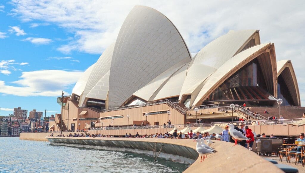 cropped-pexels-photo-2845013-2845013.jpg Sydney Opera House with tourists and waterfront view on a sunny day.