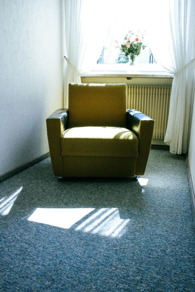 Minimalist interior featuring a cozy armchair and flower vase by a sunlit window.