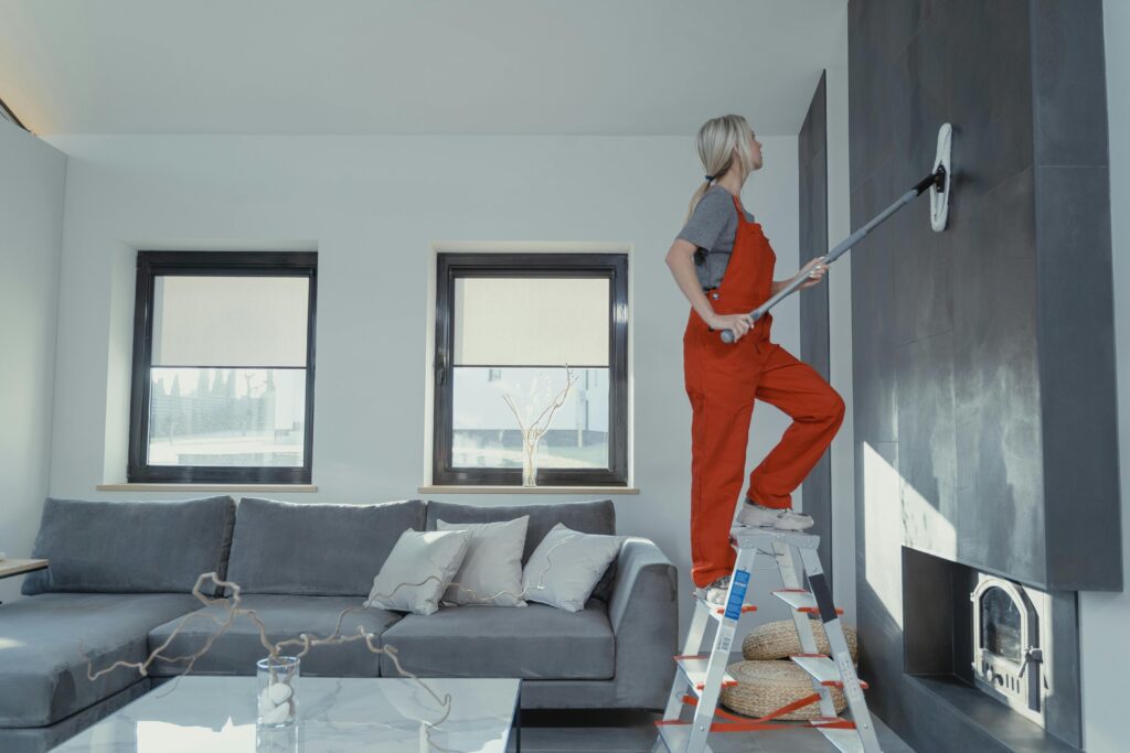 pexels-photo-6195284-6195284 A woman in overalls cleans a wall in a stylish living room, enhancing home hygiene.