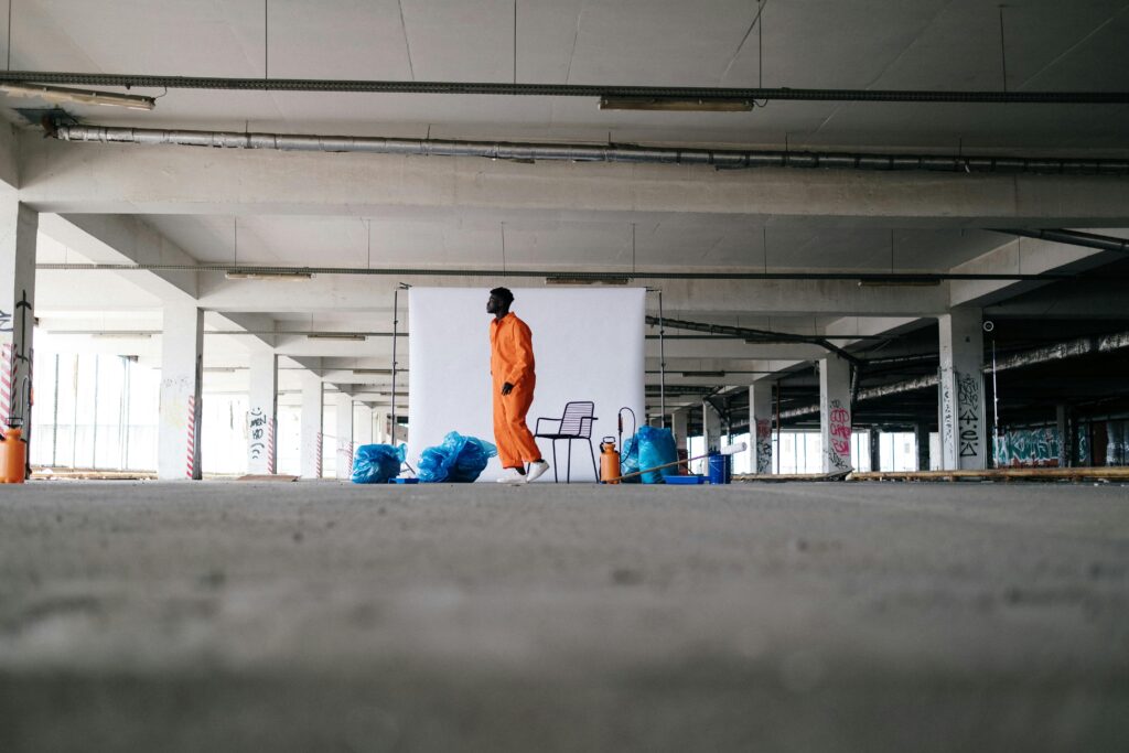 pexels-photo-9222193-9222193 A man in orange overalls stands with trash bags in an urban parking garage.