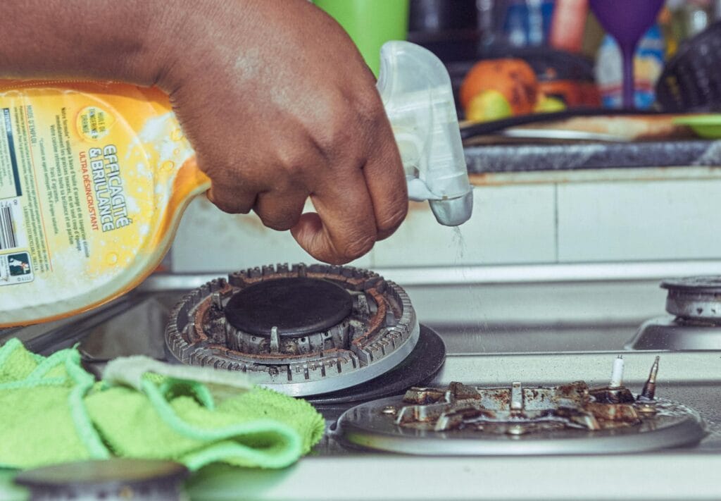 pexels-photo-14215010-14215010 A detailed view of a hand cleaning a stovetop using a spray bottle and cloth.