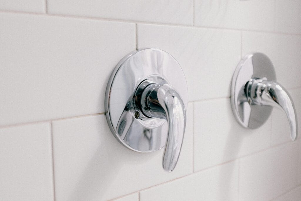pexels-photo-3758497-3758497 Close-up of chrome handles on a white tiled bathroom wall, capturing elegance and hygiene.