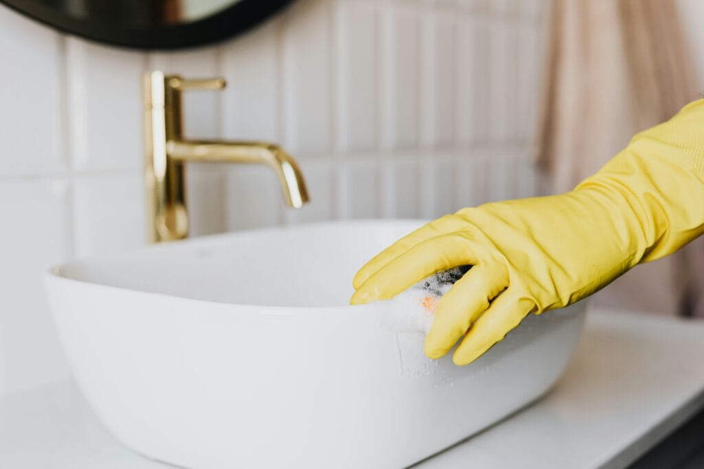 pexels-photo-4239114-4239114 Crop faceless person in yellow latex protective glove cleaning surface of white stylish sink in contemporary bathroom interior