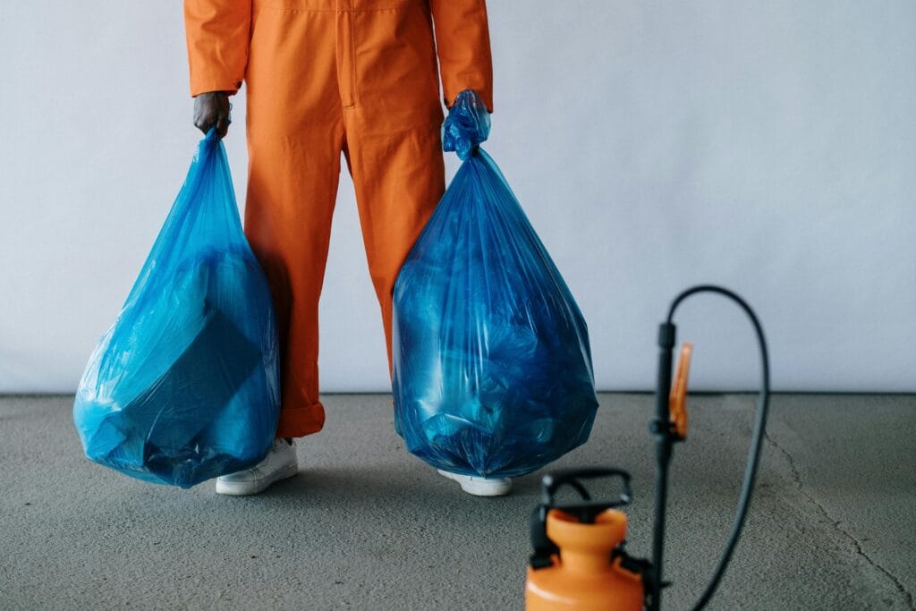 pexels-photo-9222613-9222613 Sanitation worker in orange overalls holding blue trash bags indoors for waste management.