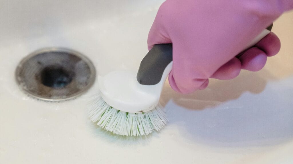 pexels-photo-9462652-9462652 A close-up of a hand in a glove cleaning a sink with a scrub brush.